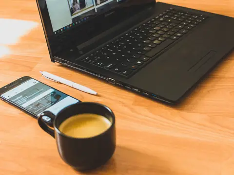 A laptop, a phone and a cup of coffee on a wooden desk