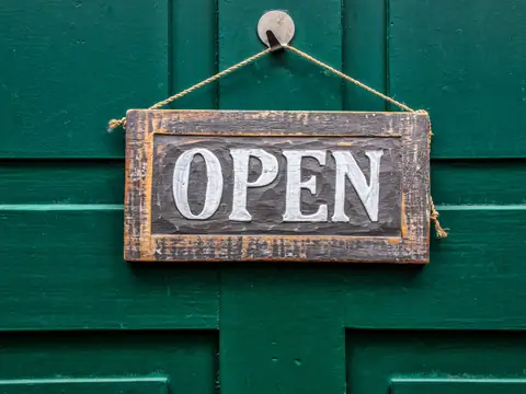 A wooden open sign hanging on a green door