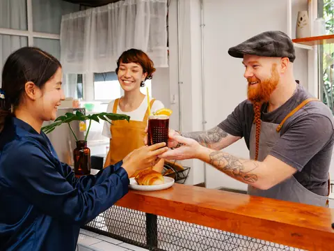 A cafe owner handing drinks to customers across the counter