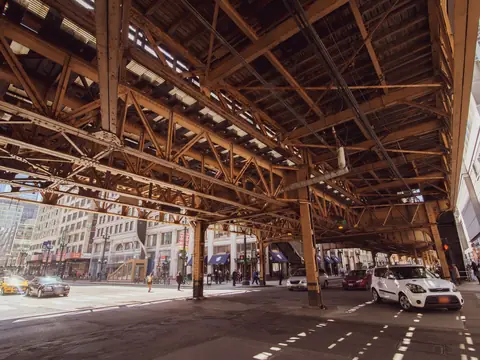 Cars and people under the elevated 'L' tracks on a sunny Loop street