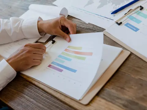 Hands turning the pages of a printed chart report on a desk