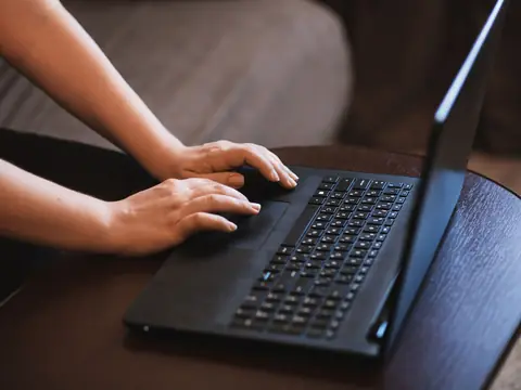 Hands typing on a laptop on a dark wooden table