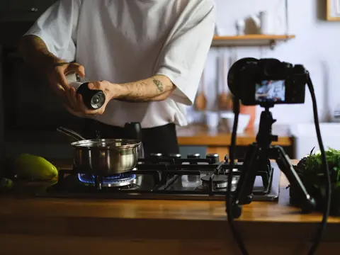A cook seasoning a pot on the stove while a camera on a tripod films