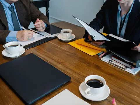 Two people going through papers over coffee at a wooden table