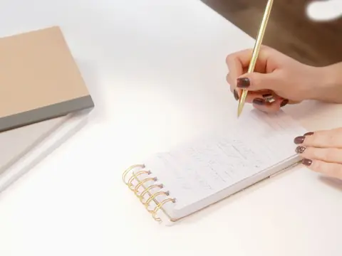 A hand writing notes on a small spiral notepad