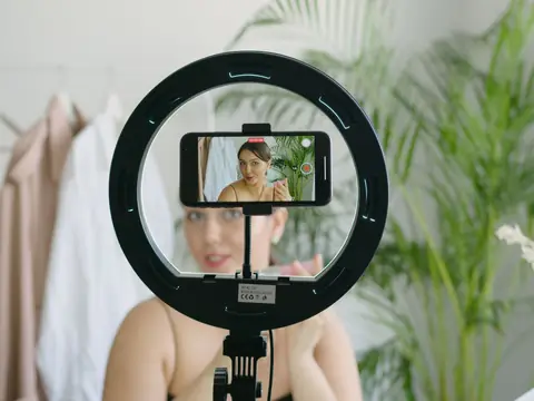 A phone in a ring light filming a woman in a bright room