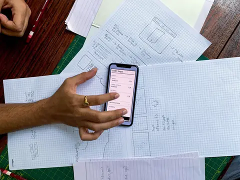 A hand holding a phone over paper website sketches