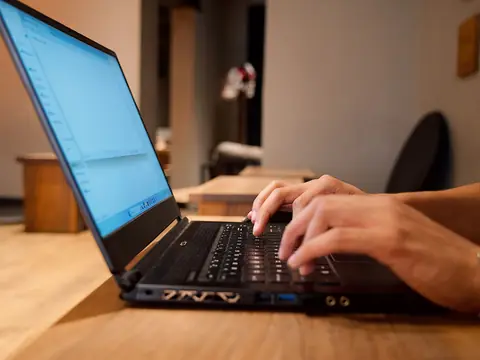 Hands typing on a laptop at a wooden table