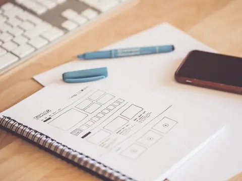 A notebook with website wireframe sketches beside pens and a phone