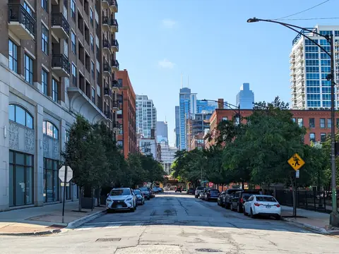 A tree-lined Chicago street with parked cars and the skyline beyond