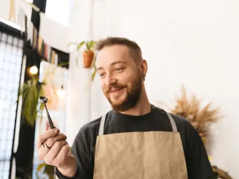 A smiling man in an apron holding a small tool in a bright studio